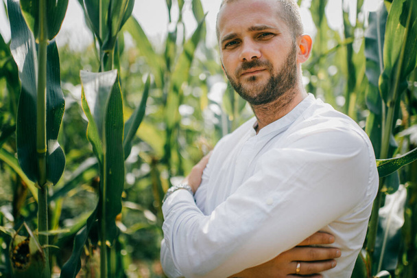 Beautiful young caucasian man in white shirt, blue jeans and white boots goes for a walk in the cornfield. - Foto, Bild