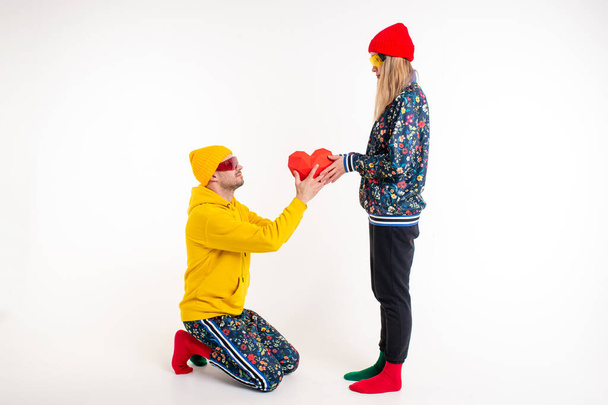 Stylish man gifting a heart to girlfriend in colorful clothes over white background - Photo, Image