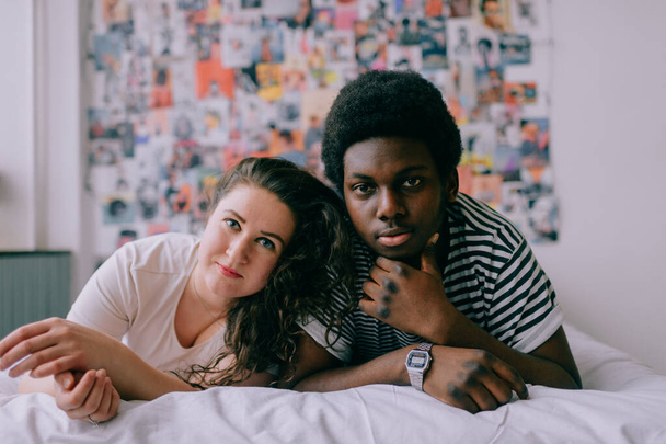 Loving interracial couple relaxing on white bed over 90s style background - Фото, изображение