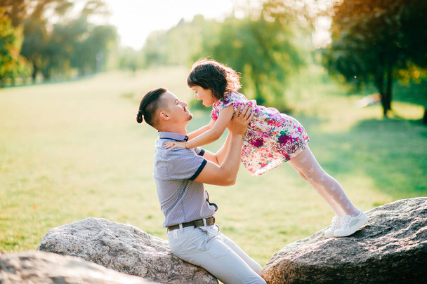 Dad and daughter summer outdoor activity. Loving father adore his lovely playful cheerful baby. Parent and child have fun in park. Little girl falling down at father. Happy family lifestyle portrait - Fotó, kép
