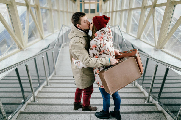 Lifestyle couple of young happy lovers carry vintage brown suitcases at railway station. Pair of stylish cheerful hipsters going down the stairs.  Handsome man travel with his lovely girlfriend - Фото, зображення