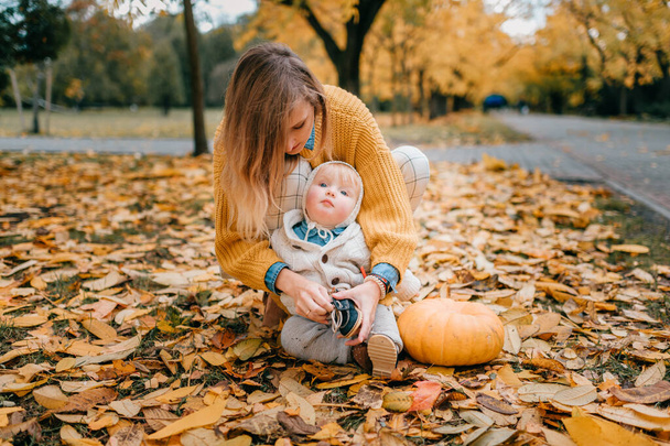 Lovely caucasian mother in yellow blouse and white trousers spends free time in the autumn park with her child with red hair, big blue eyes and pump lips - Foto, immagini
