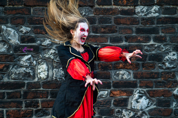 Quaint female in witch costume with an ominous expression of his face is engaged in magic and conjures putting her hands forward against the background of the brick wall - Foto, afbeelding