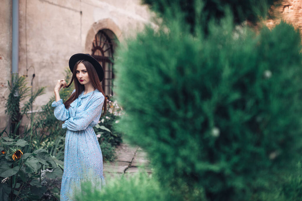 Long haired brunette girl in bintage blue dress posing in green garden in french style - Foto, Imagem