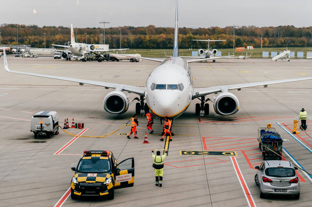COLOGNE, GERMANY - NOVEMBER 16, 2017: Koln Bonn airport employees  service landed airplane. View from waiting room through window at runway with aircraft and maintenance staff in work flow - Foto, Imagem
