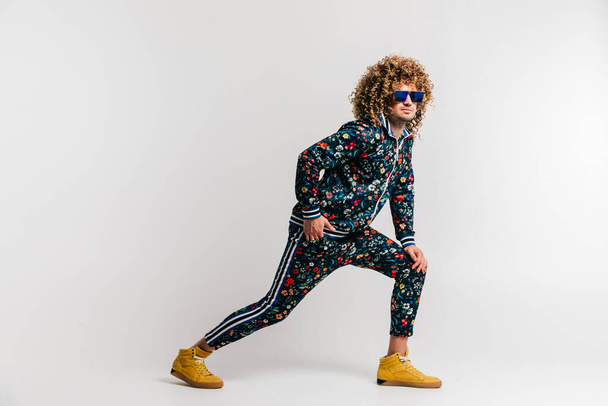 Adult positive smiling funky man with curly hair style in suglasses and vintage clothes posing on white studio background. Funny portrait of stylish male person. 80s fashion. Unusual eccentric guy - Photo, Image