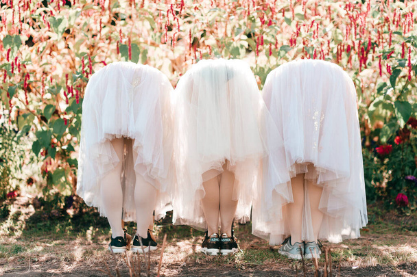 Three flexible ballet dancers stretching out from behind in white tutu over flowers in sunny park. - Fotó, kép