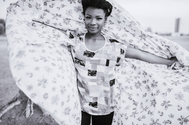 Cheerful dark skinned girl with hands apart holding sheet with floers print outdoor - Φωτογραφία, εικόνα