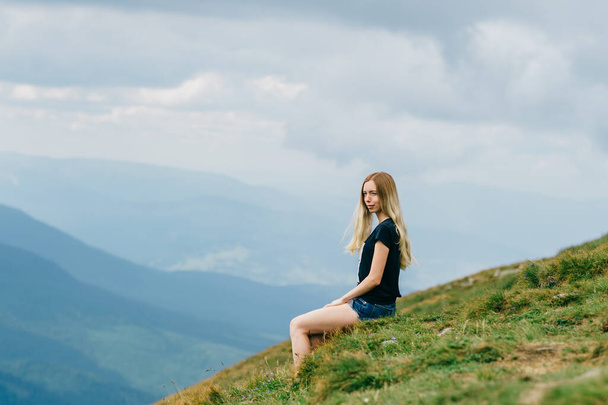 Young girl relaxing and enjoying scenic view on top of mountain.  Bliss, happiness. Beautiful summer nature landscape. Lonely young blonde teen traveler dreaming outdoor on vacation.  Romantic mood - Photo, Image