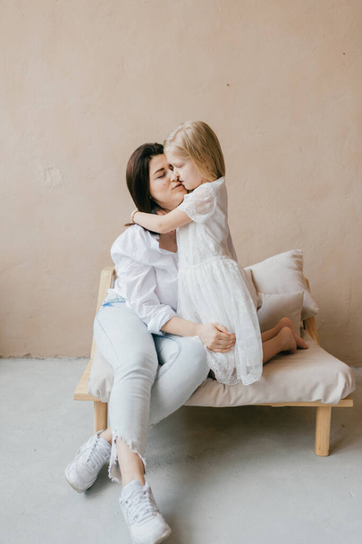 Mother and daughter indoor lifestyle portrait. Mom with child have fun in studio on yellow wall. Happiness of motherhood. Mother hugs with her little daughter. Young emotional girl  embraces her mom - Foto, immagini