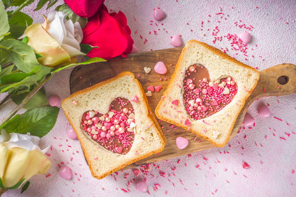 Słodka kanapka na śniadanie. Kreatywny pomysł na Walentynkową przekąskę lub lunch. Kanapka z tostem z masłem orzechowym i makaronem czekoladowym, z sercami Valentine czerwony i różowy cukier posypka widok z góry. - Zdjęcie, obraz