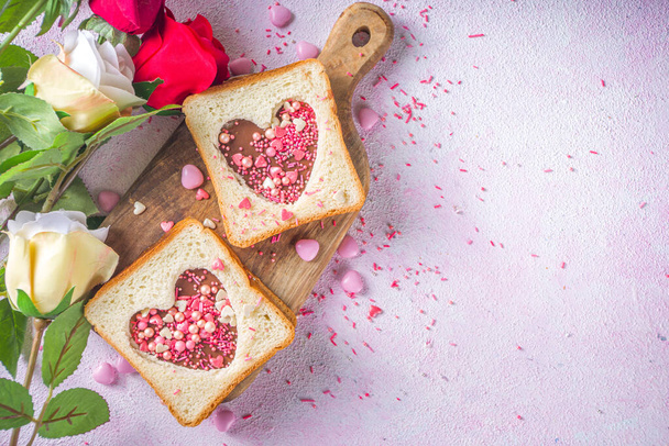 Słodka kanapka na śniadanie. Kreatywny pomysł na Walentynkową przekąskę lub lunch. Kanapka z tostem z masłem orzechowym i makaronem czekoladowym, z sercami Valentine czerwony i różowy cukier posypka widok z góry. - Zdjęcie, obraz