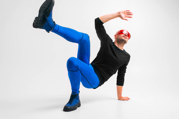 Fashion portrait of stylish man in blue tights and indigo boots stretching and exercising over white studio background. - Фото, зображення