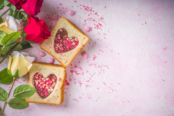 Cute sweet breakfast sandwich. Creative idea for Valentine day snack or lunch. Toast sandwich with peanut butter and chocolate pasta, with Valentine hearts red and pink sugar sprinkles top view. - Fotografie, Obrázek