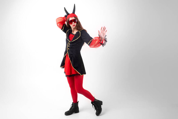 Sexy brunette girl in red tights, masquerade costume, futuristic glasses and devil horns on her head posing with passion over white background - Foto, afbeelding