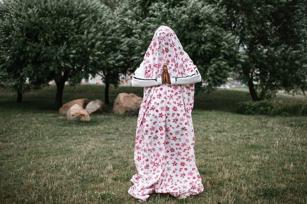 Dark skinned man in ghost costume standing in green field in park - Fotografie, Obrázek