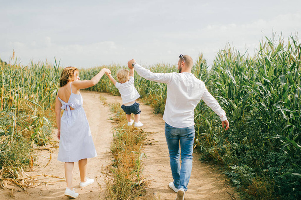 Cheerful family of three have a lot of fun together in the big cornfield in hot summer morning. - Foto, Imagem