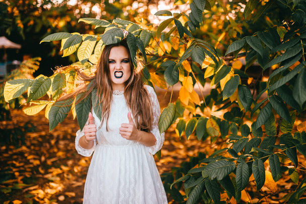 Beautiful girl with gothic make up and funny face expression posing in summer park  - Photo, image