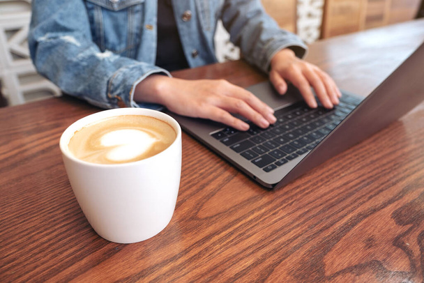 Close-up beeld van de handen van de vrouw met behulp van en typen op laptop computer toetsenbord met koffiekopje op de tafel - Foto, afbeelding