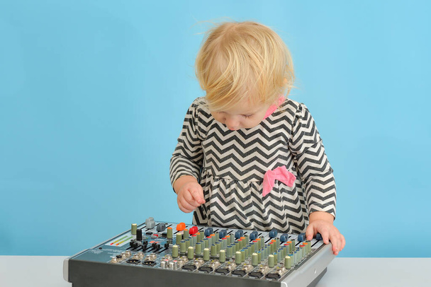 Una niña pequeña presiona botones en una consola de mezclas de música. - Foto, imagen