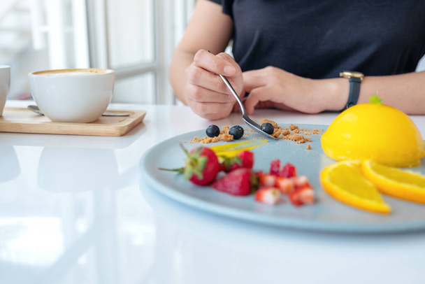 A woman eating orange cake with mixed fruit by spoon in cafe - Foto, Imagen