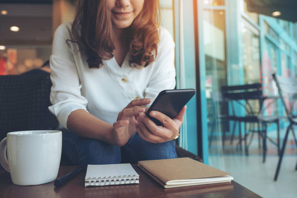 Imagen de cerca de una mujer sosteniendo, usando y señalando el teléfono inteligente en la cafetería - Foto, Imagen