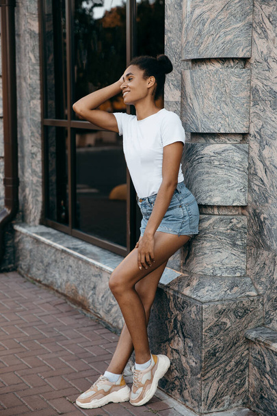 ritratto di attraente donna afro americana su pantaloncini e t-shorts su sfondo grigio  - Foto, immagini