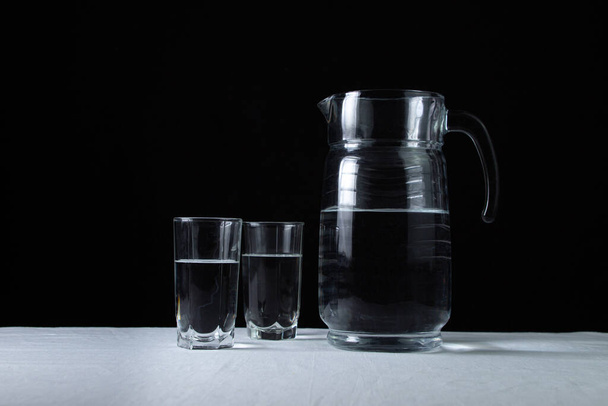 Öntözés vízzel, fekete háttérrel. Egy kancsó és két pohár vízzel töltve. Tiszta ivóvíz. Ökológia tisztasági koncepció. - Fotó, kép