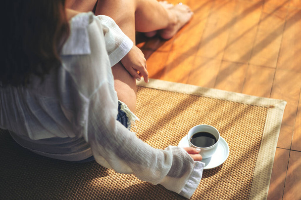 Вид сверху на женщину, сидящую и держащую чашку горячего кофе на полу утром - Фото, изображение