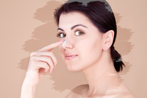 Girl touching her nose with cream (profile) on a beige background, unusual toning - Photo, Image