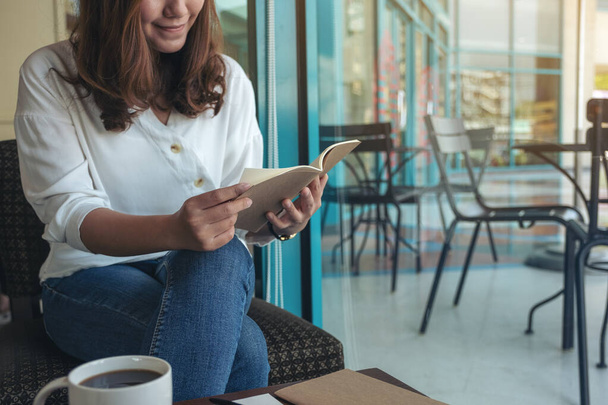 Imagen de cerca de una mujer abriendo un libro para leer con cuadernos y taza de café en la mesa de madera en la cafetería  - Foto, Imagen