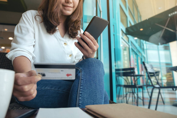 Image rapprochée d'une femme tenant une carte de crédit et utilisant les services bancaires mobiles alors qu'elle était assise dans un café - Photo, image