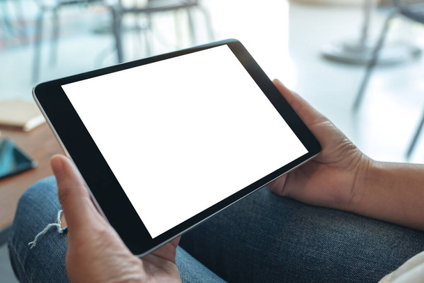Mockup immagine di una donna seduta e con in mano tablet pc nero con schermo bianco vuoto desktop orizzontalmente - Foto, immagini