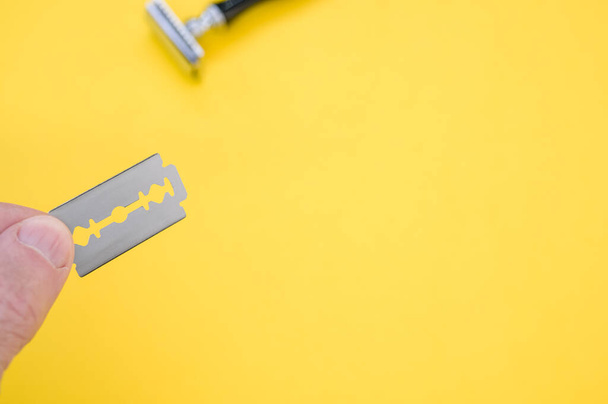 A hand holding blade with a mechanical razor on the background against a yellow surface - Φωτογραφία, εικόνα