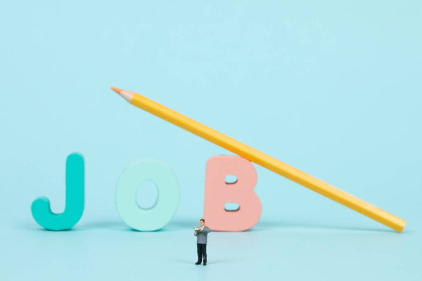 A closeup of a people figurine and the word "job" with a yellow pencil in the background - 写真・画像