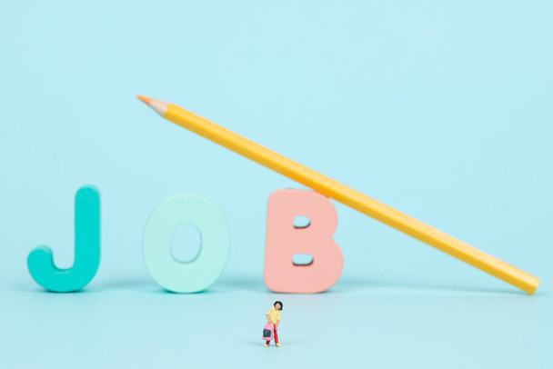 A closeup of a people figurine and the word "job" with a yellow pencil in the background - Fotoğraf, Görsel