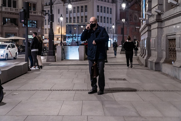 MADRID, SPANYOLORSZÁG - December 26, 2020: Álarcos férfi beszél telefonon az Alcala utcán Madridban éjszaka - Fotó, kép