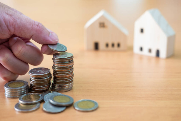 Selective focus at men hand while put coin into stack with blurred house mock up at the background. Saving plan and set goal for house ownership. Property investment concept. - Photo, Image