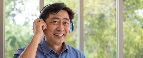Banner, panorama shot of senior Asian grandfather enjoy and feeling happy while listening music from wireless headphone that streaming music from smartphone or tablet device. Elderly lifestyle. - Photo, Image