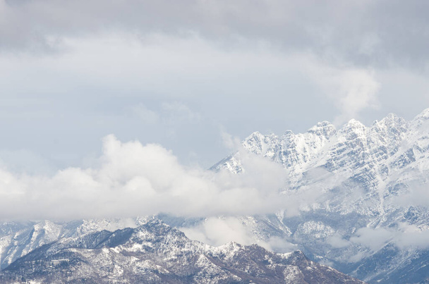 The beautiful scenery of a high rocky mountain covered with snow under a cloudy sky - Photo, Image
