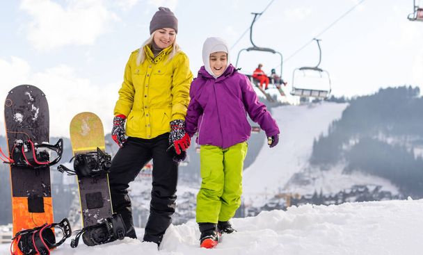 mother and daughter with snowboards at winter resort - Photo, Image