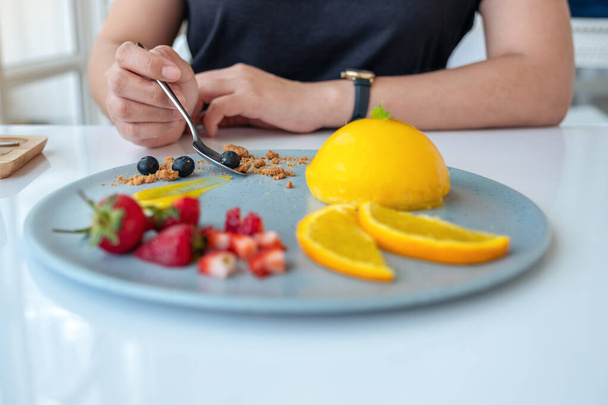 Una mujer comiendo pastel de naranja con fruta mezclada por cuchara en la cafetería - Foto, Imagen