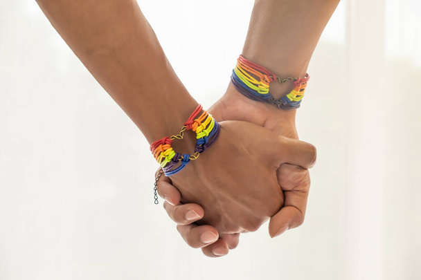Detailní záběr asijského páru mužů držící se za ruce s gay hrdostí duha povědomí náramky. LGBT, láska stejného pohlaví a homosexuální vztahy s kopírovacím prostorem. - Fotografie, Obrázek