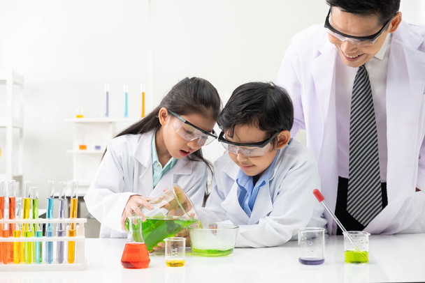 Genç Asyalı erkek ve kız gülümsüyor ve sınıfta öğretmenle laboratuarda fen deneyleri öğrenirken eğleniyorlar. Bilimsel ekipman ve tüplerle çalış. Eğitim kavramı. - Fotoğraf, Görsel