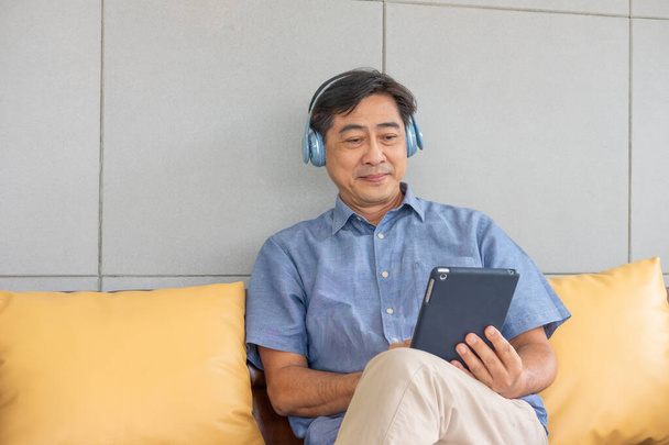 Senior Asian grandfather enjoy and feeling happy while listening music from wireless headphone that streaming music from smartphone or tablet device. Elderly retirement lifestyle with good health. - Photo, Image