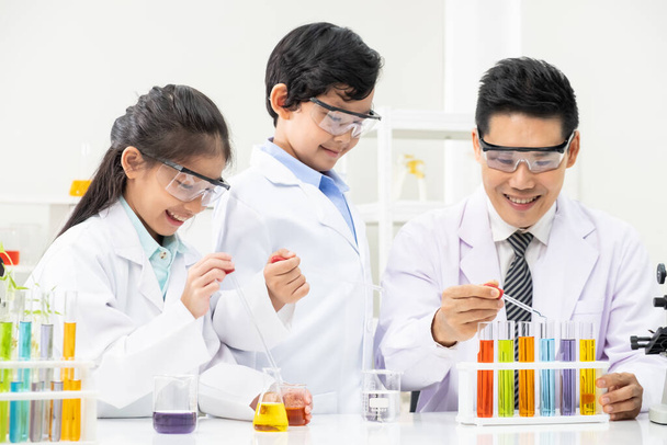 Young Asian boy and girl smile and having fun while learning science experiment in laboratory with teacher in classroom. Study with scientific equipment and tubes. Education concept. - Photo, Image