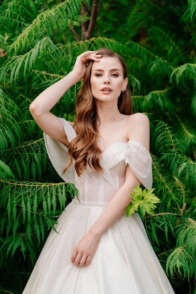 beautiful woman in a white dress posing in against of green leaves. - Foto, Imagem