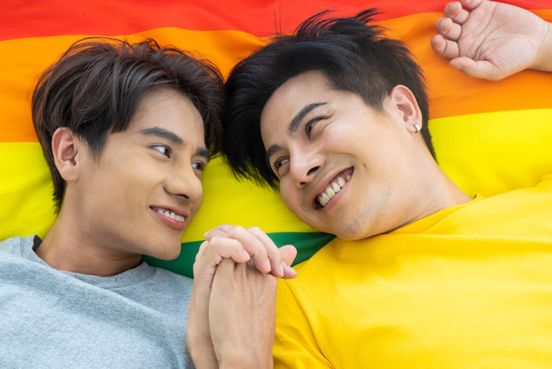 Portret van een jong homoseksueel stel dat samen op het bed ligt met een kleurrijke vlag op de achtergrond. Geluksmoment van biseksueel. Gendergelijkheid en mensenrechtenconcept. - Foto, afbeelding