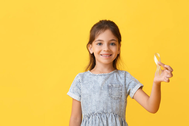 Klein meisje met gouden lint op kleur achtergrond. Bewustmakingsconcept voor kinderkanker - Foto, afbeelding