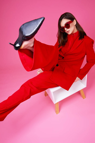 Fashion model in red suit and sunglasses. Studio shot. - 写真・画像